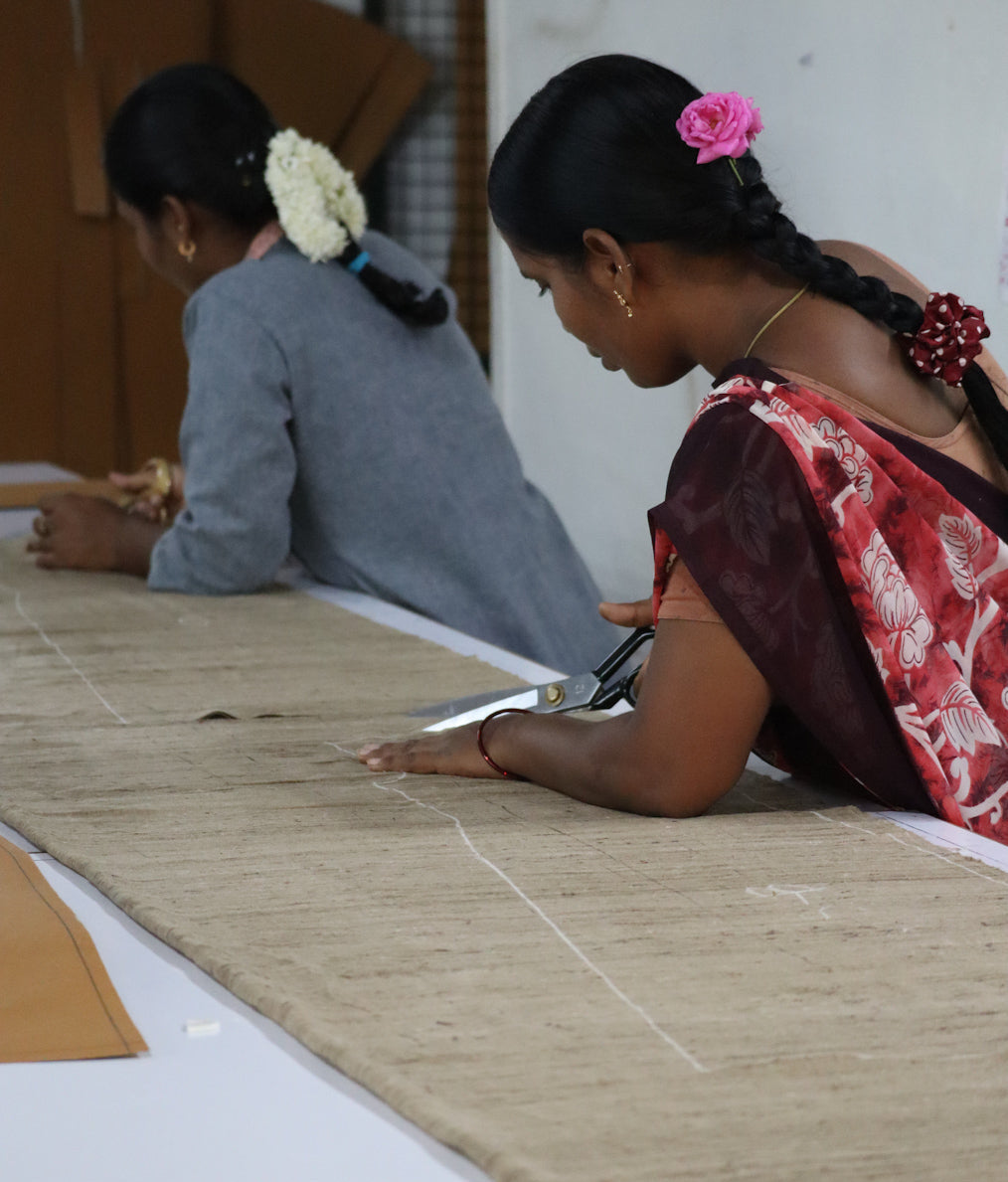 Two women working with fabric on a table, one cutting fabric with scissors.