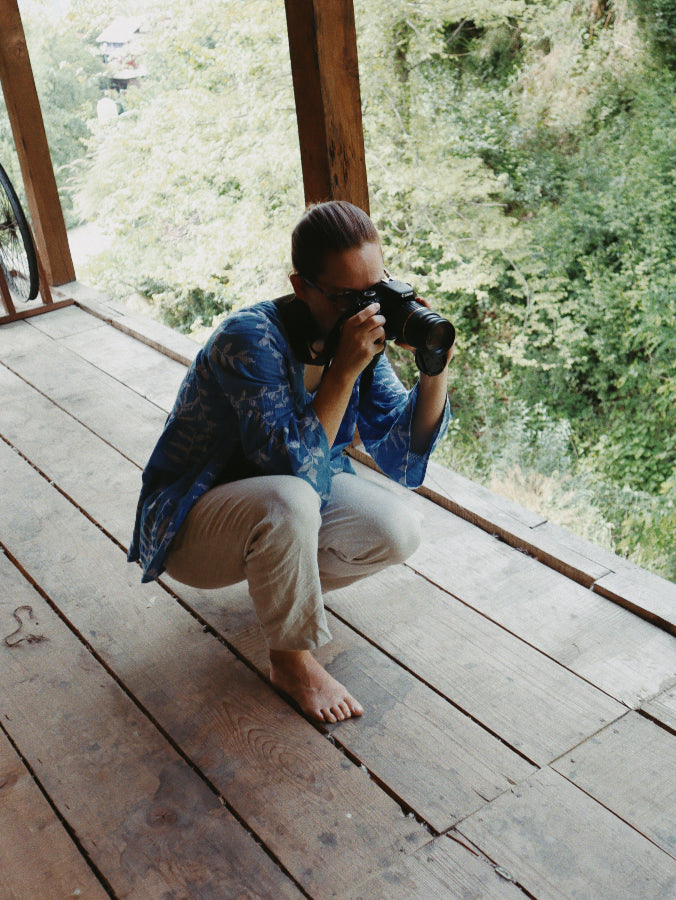 Nüwa Mano founder taking photos with camera on a wooden deck with green forest background behind her