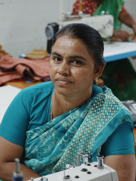Woman in a blue sari sitting at a sewing machine with a blurred background