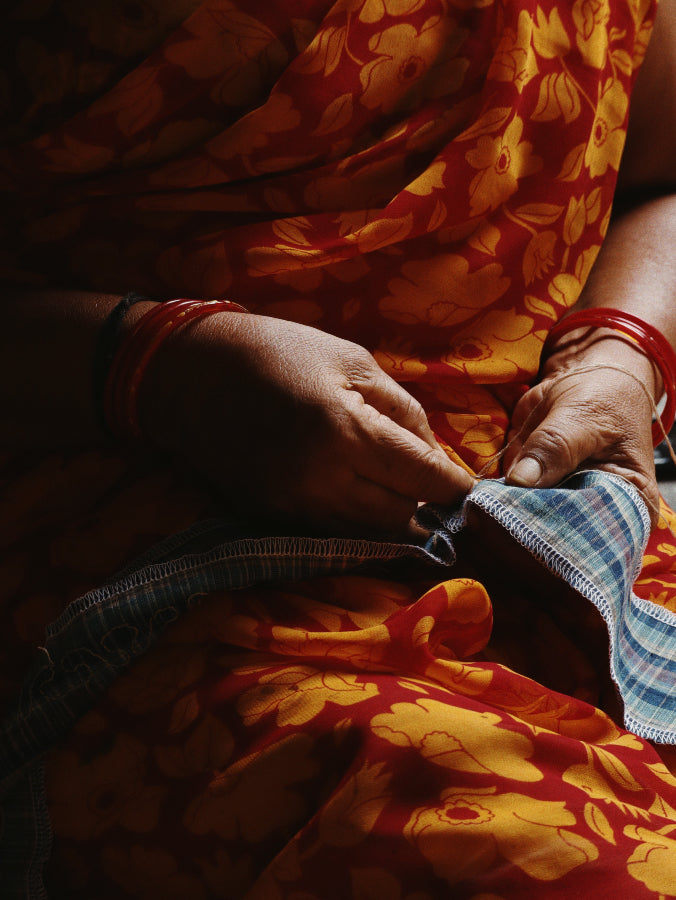 A lady in an orange sari hand embroidering a Nüwa Mano design
