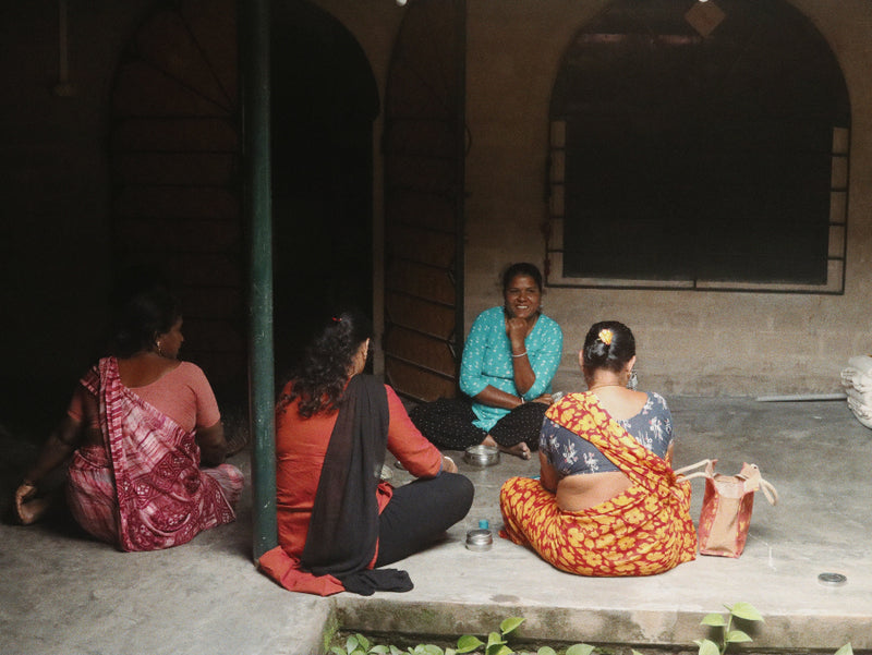 Four women sitting on a stone ledge in a dimly lit outdoor setting.