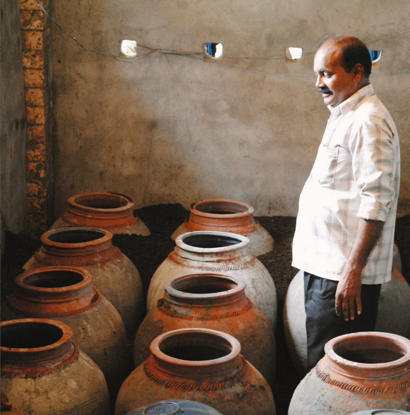 Man standing next to large clay pots in a room with a rustic wall.