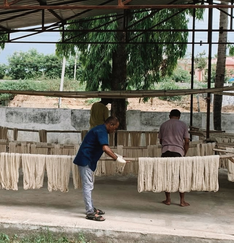 Three people working with cotton yarn  in an outdoor setting.